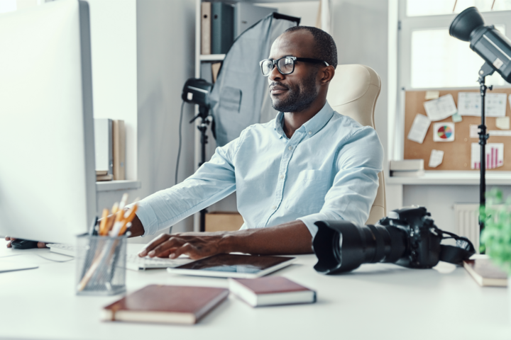 Handsome young man using computer to find best contact management system while working in the modern office